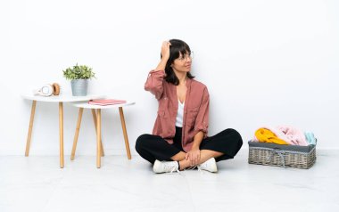 Genç melez kadın, beyaz arka planda izole bir şekilde yerde oturmuş giysilerini katlıyor.