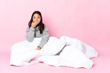 Genç, melez, pijama giymiş bir kadın yerde oturup ağızlarını eliyle kapatıyor.