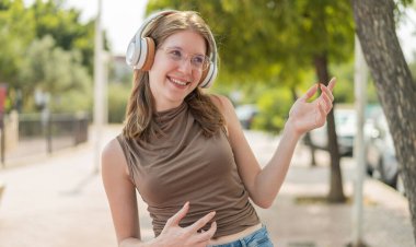 Açık havada gözlüklü genç bir Fransız kız müzik dinliyor ve gitar jesti yapıyor.