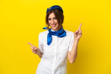 Sarı arka planda izole edilmiş uçak hostesi kadın parmak uçlarını işaret ediyor ve mutlu.