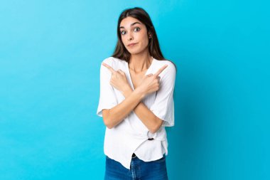 Mavi arka planda izole edilmiş genç beyaz kadın, yan taraftakilerin şüphelerine işaret ediyor.