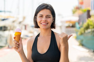 Açık havada kornet dondurması olan genç ve güzel Bulgar kadın bir ürün sunmak için kenarı işaret ediyor