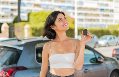 Genç, güzel Bulgar kadın elinde araba anahtarlarıyla dışarı bakıp gülümsüyor.