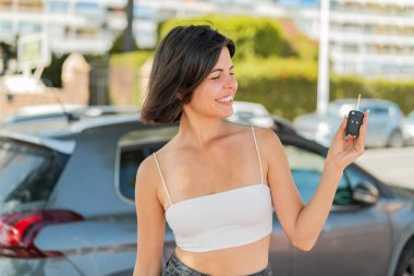 Genç, güzel Bulgar kadın elinde arabanın anahtarlarını tutarken neşeli bir ifade takınıyor.