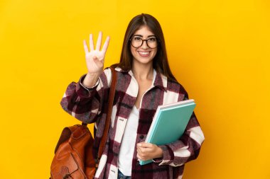 Sarı arka planda izole edilmiş genç bir bayan mutlu ve parmaklarıyla dört kişi sayıyor.