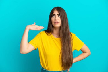 Kafkasyalı genç bir kadın mavi arka planda izole edilmiş, yorgun ve hasta bir ifadeyle.