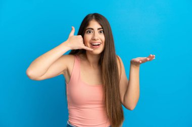 Kafkasyalı genç bir kadın mavi arka planda izole edilmiş telefon jestleri yapıyor.