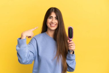 Mavi arka planda saç fırçası tutan beyaz bir kadın baş parmak işareti yapıyor.