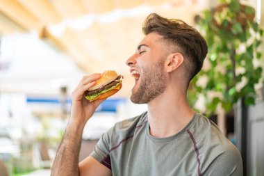 Elinde hamburger tutan genç yakışıklı adam.