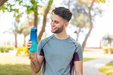 Açık havada bir şişe su ve neşeli bir ifadeyle genç yakışıklı sporcu.