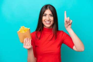 Mavi arka planda izole edilmiş patates kızartması yakalayan beyaz bir kadın harika bir fikre işaret ediyor.