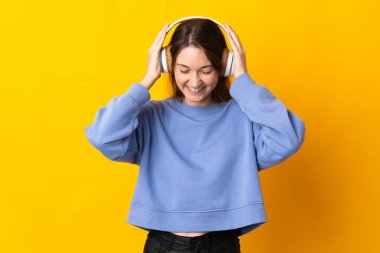 Sarı arka planda izole edilmiş genç İrlandalı kadın müzik dinliyor.