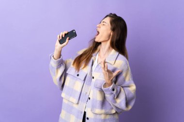 Genç İrlandalı kadın, mor arka planda cep telefonu ve şarkı söyleyerek izole edilmiş.