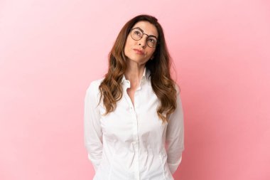 Orta yaşlı beyaz kadın pembe arka planda izole edilmiş ve yukarı bakıyor.