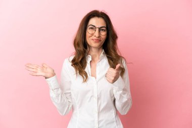 Orta yaşlı beyaz bir kadın pembe arka planda izole edilmiş. Elinde bir reklam vermek ve onaylamak için fotokopi odası hayali var.