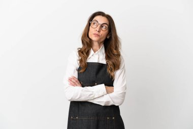 Restorandaki orta yaşlı garson kadın, beyaz arka planda izole edilmiş. Omuzlarını kaldırırken şüpheyle hareket ediyor.