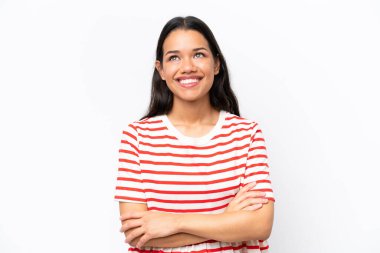 Genç Kolombiyalı kadın beyaz arka planda izole edilmiş gülümserken yukarı bakıyor