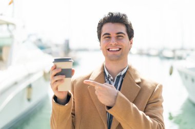 Genç yakışıklı bir adam açık havada kahve tutuyor ve onu doğrultuyor.