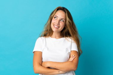 Mavi arka planda izole edilmiş genç sarışın kadın gülümserken yukarı bakıyor.