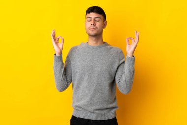 Zen pozisyonunda sarı arka planda izole genç Kolombiyalı adam