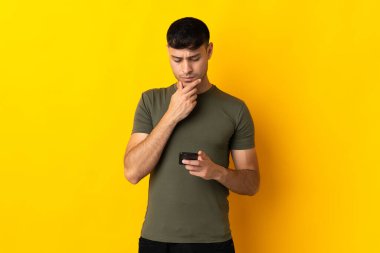 Genç Kolombiyalı adam sarı arka planda izole edilmiş düşünüyor ve bir mesaj gönderiyor.