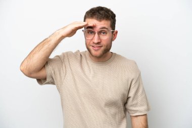 Beyaz arka planda izole edilmiş genç beyaz bir adam bir şeye bakmak için çok uzaklara bakıyor.