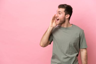 Pembe arka planda izole edilmiş genç beyaz adam ağzı sonuna kadar açık bağırıyor.