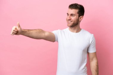 Pembe arka planda izole edilmiş genç beyaz bir adam baş parmak hareketi yapıyor.