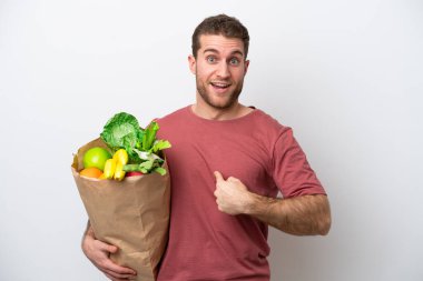 Beyaz arka planda izole edilmiş bir alışveriş torbası tutan beyaz bir adam. Sürpriz bir yüz ifadesi var.