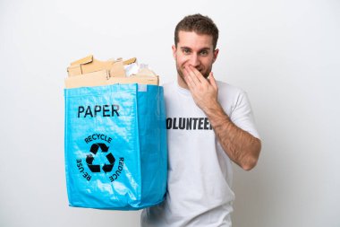 Beyaz arka planda izole edilmiş bir şekilde geri dönüşüm için kağıt dolu bir çanta tutan beyaz bir adam mutlu ve gülümseyen bir ağızla elini kapatıyor.