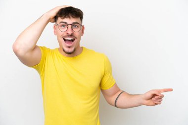 Beyaz arka planda izole edilmiş beyaz tenli yakışıklı bir adam şaşırmış ve parmağıyla kenarı işaret ediyor.