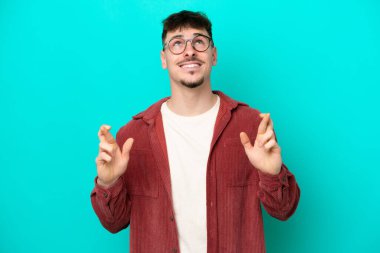 Beyaz tenli yakışıklı adam mavi arka planda izole edilmiş, şans diliyor ve en iyisini diliyor.