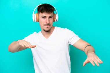Beyaz tenli yakışıklı adam mavi arka planda izole edilmiş müzik ve dans dinliyor.
