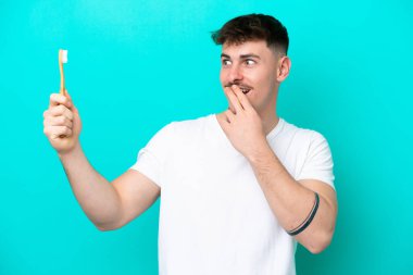 Mavi arka planda diş fırçalayan beyaz bir genç. Şaşırmış ve şok olmuş bir yüz ifadesi var.