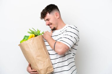 Beyaz arka planda izole edilmiş bir alışveriş poşeti taşıyan genç beyaz bir adam omuz ağrısından muzdarip.