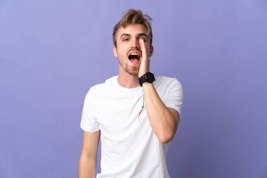 Mor arka planda izole edilmiş, ağzı açık genç sarışın adam bağırıyor.