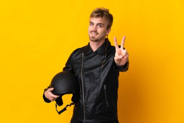 Sarı arka planda izole edilmiş motosiklet kasklı bir adam gülümsüyor ve zafer işareti gösteriyor.