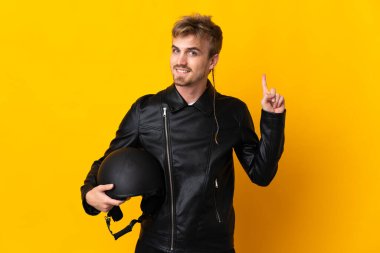Sarı arka planda izole edilmiş motosiklet kasklı bir adam en iyinin işareti olarak parmağını kaldırıyor.