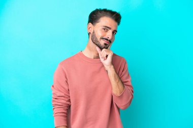 Kafkasyalı genç bir adam mavi arka planda izole edilmiş bir fikir düşünüyor.