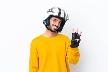 Beyaz arka planda izole edilmiş motosikletli beyaz kasklı genç beyaz adam mutlu ve parmaklarıyla üçe kadar sayıyor.