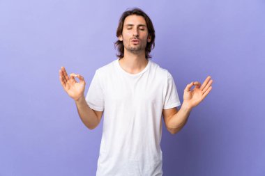 Mor arka planda, Zen pozisyonunda izole genç yakışıklı bir adam.