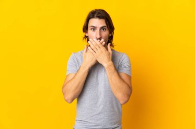 Sarı arka planda izole edilmiş genç ve yakışıklı bir adam elleriyle ağzını kapatıyor.