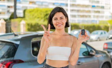 Dışarıda arabanın anahtarlarını tutan genç, güzel Bulgar kadın gülümsüyor ve zafer işareti gösteriyor.