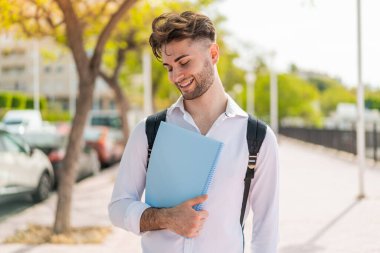 Genç ve yakışıklı bir öğrenci açık havada mutlu bir ifadeyle.