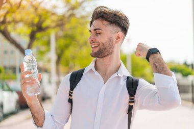Dışarıda elinde bir şişe suyla genç ve yakışıklı bir adam zaferi kutluyor.