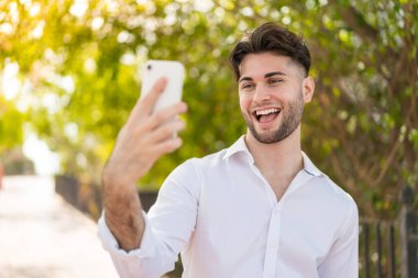 Dışarıda genç yakışıklı bir adam selfie çekiyor.