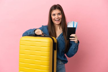 Pembe arka planda izole edilmiş genç beyaz bir kadın, bavul ve pasaportla tatilde.