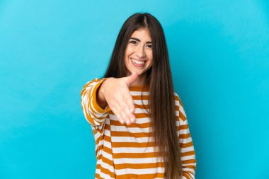 Mavi arka planda izole edilmiş genç beyaz kadın iyi bir anlaşma için el sıkışıyor.