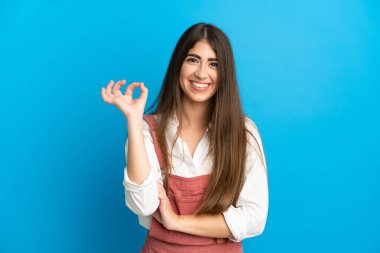 Mavi arka planda izole edilmiş beyaz bir kadın parmaklarıyla tamam işareti gösteriyor.