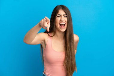 Mavi arka planda izole edilmiş genç beyaz kadın hayal kırıklığına uğramış ve ön tarafı işaret ediyor.